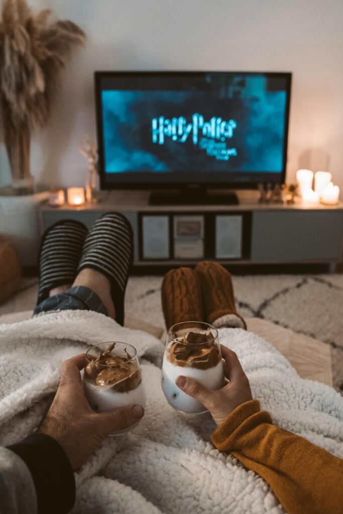 Holiday TV Deals: What to Buy & Why A couple enjoys a cozy movie night with drinks, wrapped in blankets, watching a Harry Potter film on TV.