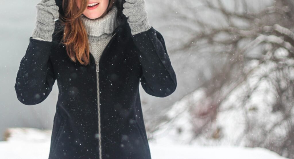 Hats, Boots, Coats, & Cozy Layers A woman enjoying a snowy winter day, dressed warmly and smiling.